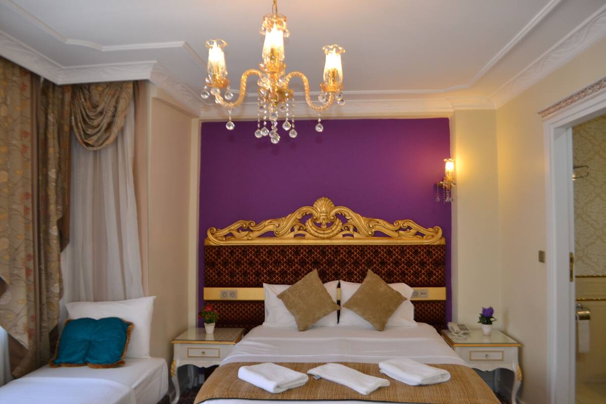 A hotel room with a large bed, a chandelier, and a purple accent wall.