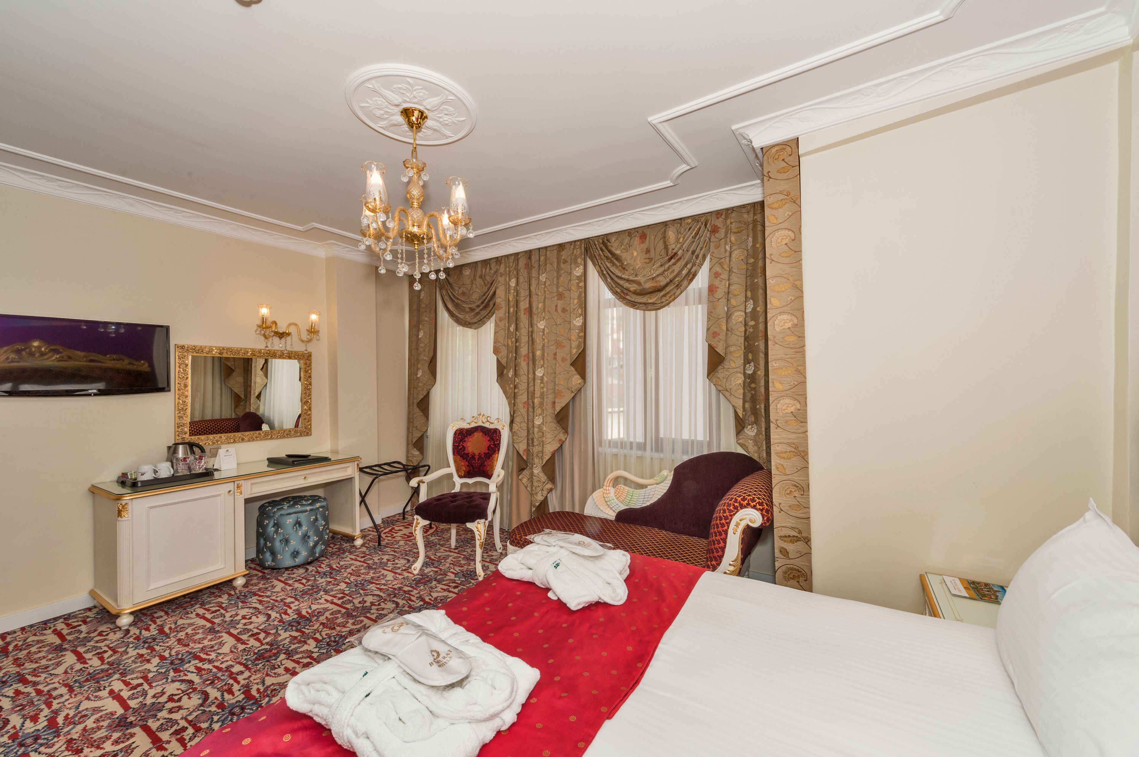Una habitación de hotel con una cama grande, un escritorio con espejo, una silla, una colcha roja y blanca y un candelabro.