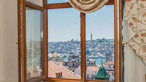 A view from a window with a wooden frame and a curtain, overlooking a cityscape with buildings and a body of water.