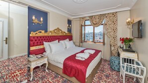 A hotel room with a large bed, a nightstand, a small table, a crib, a TV, and a window with a city view.
