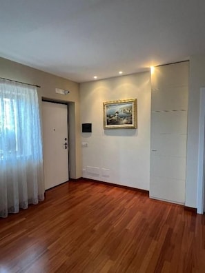 Una habitación con piso de madera, una puerta blanca, un cuadro en la pared y una lámpara.