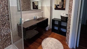 Een moderne badkamer met een douchecabine van glas, een donkere wastafel en een rond vloerkleed op de houten vloer.