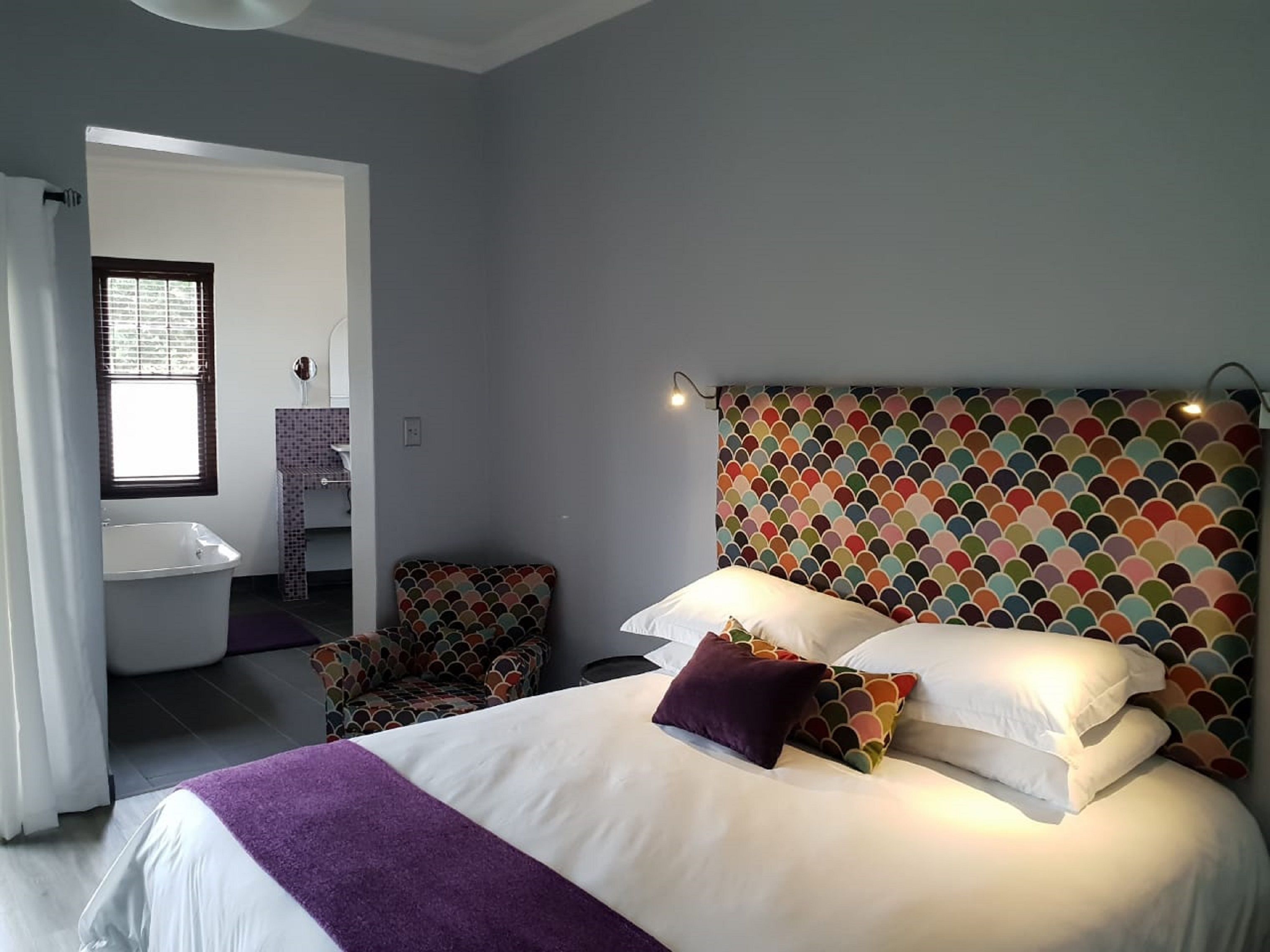 A bedroom with a bed, a chair, a bathroom with a sink, and a patterned headboard.