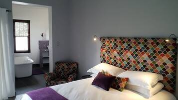 A bedroom with a bed, a chair, a bathroom with a sink, and a patterned headboard.