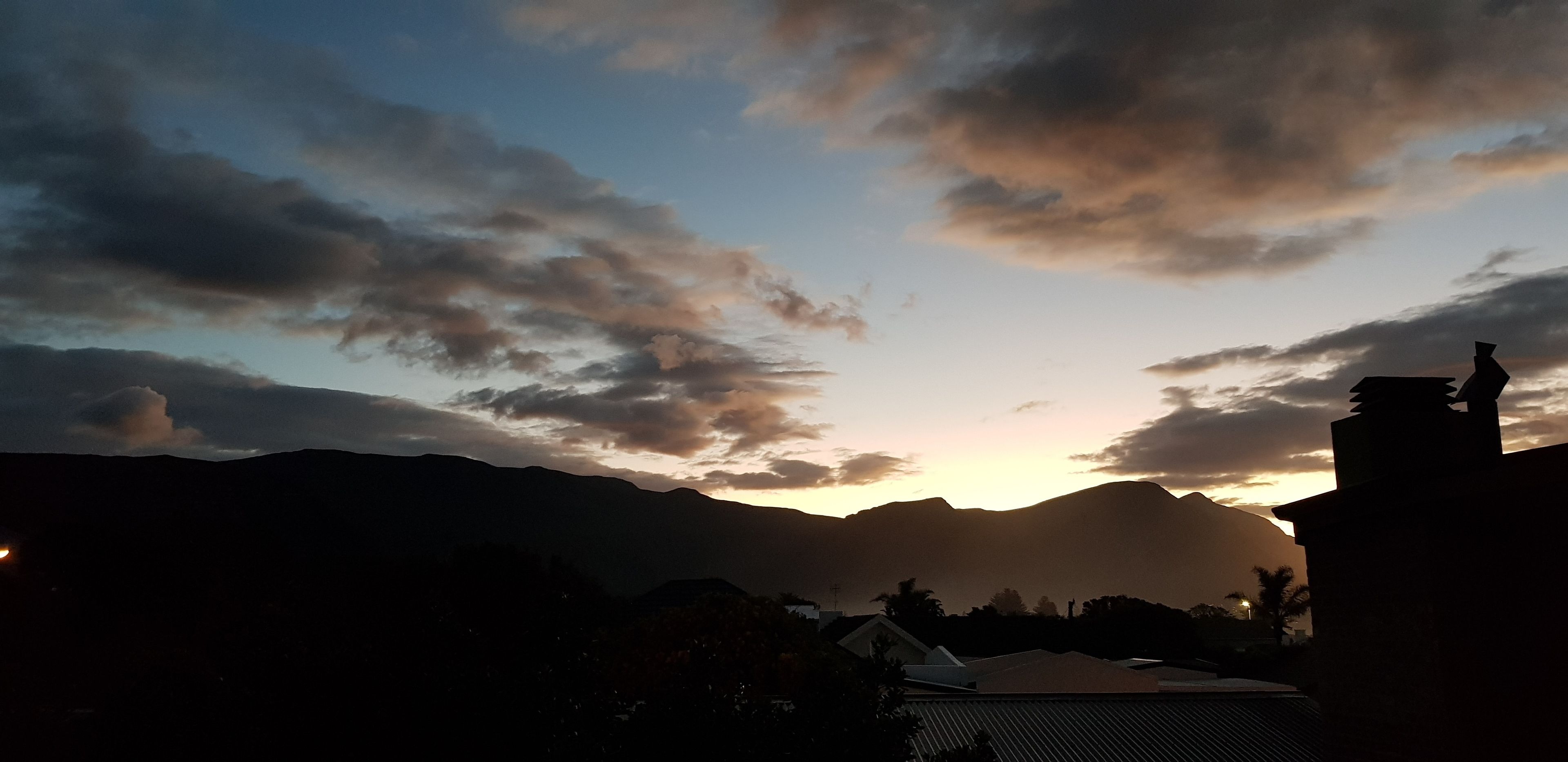 A sunset over mountains with silhouettes of buildings and a church steeple.