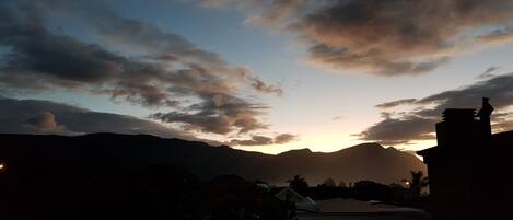 A sunset over mountains with silhouettes of buildings and a church steeple.