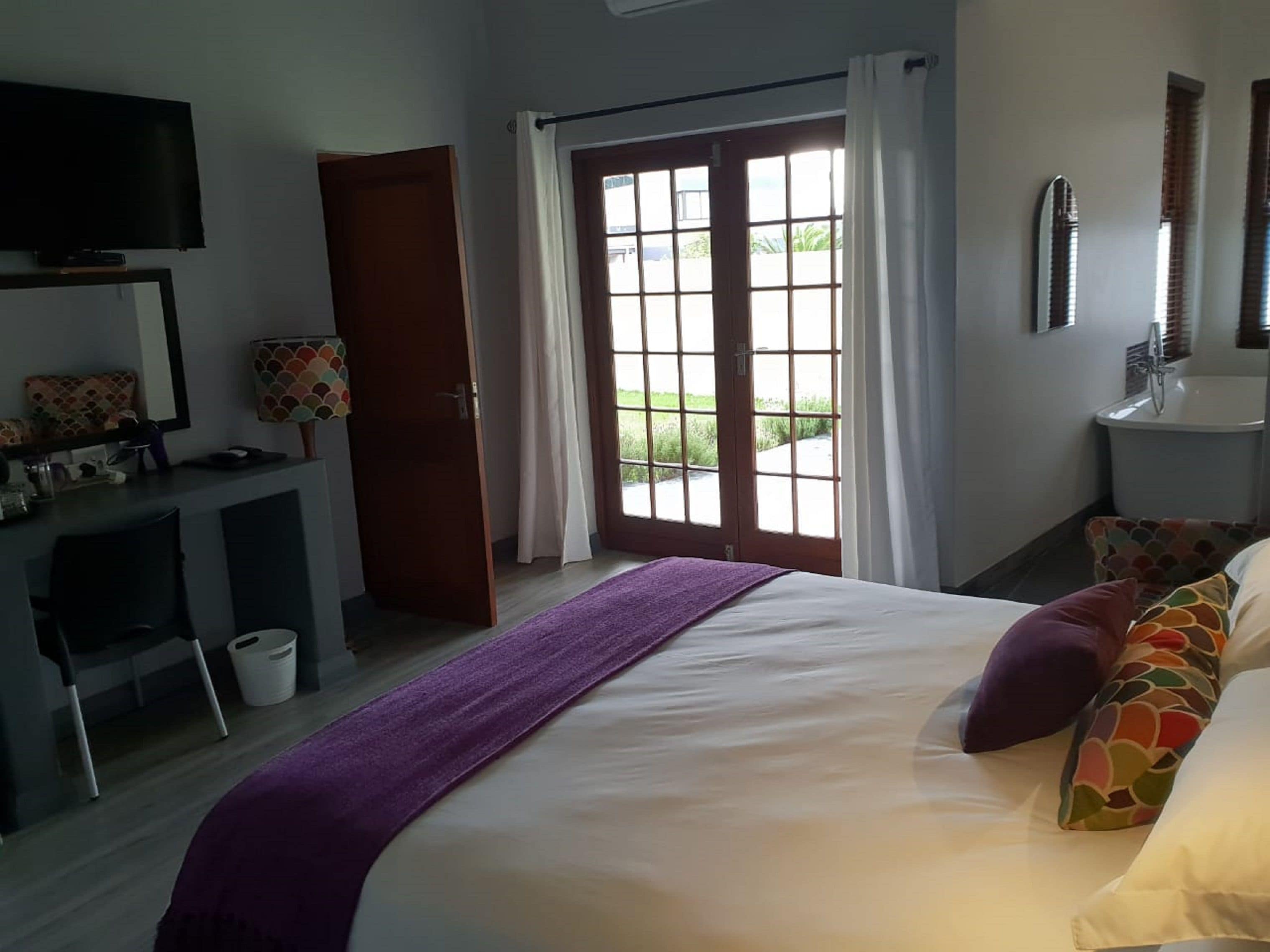 A hotel room with a bed, a desk, a television, a bathroom, and a view of the outdoors.