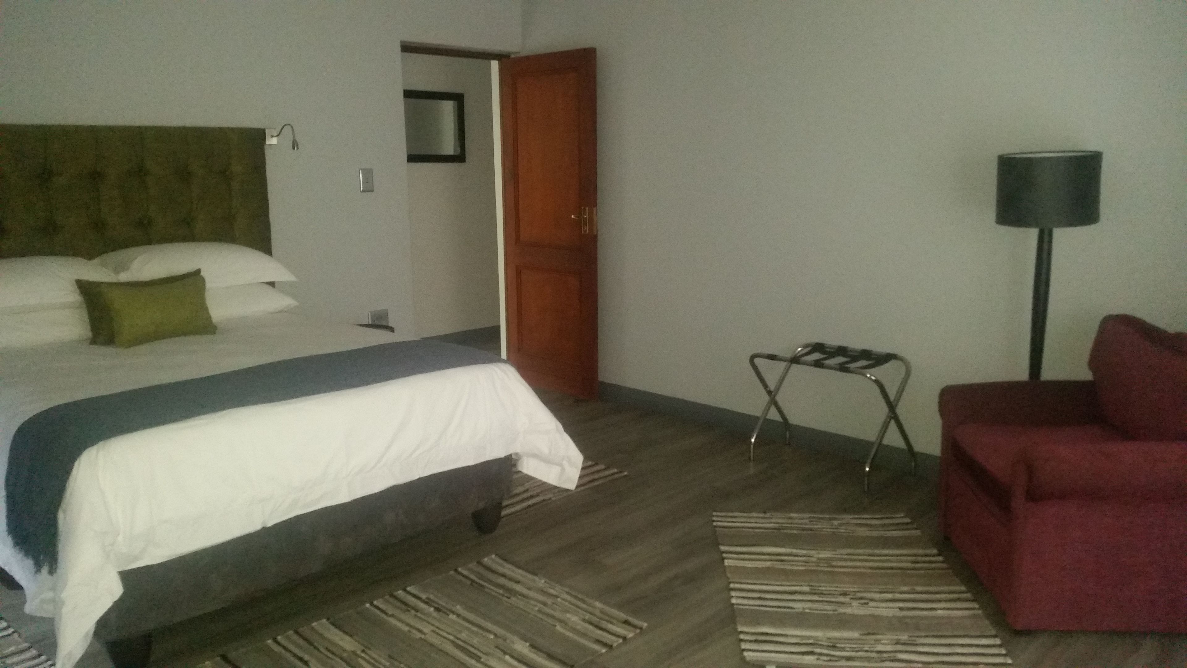 A hotel room with a bed, a red armchair, a standing lamp, and a small table.