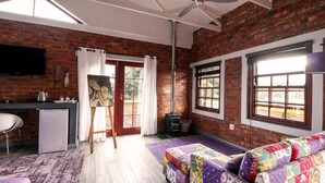 Una habitación con pared de ladrillo, cama con ropa de cama colorida, escritorio con hervidor, televisor y ventana con vistas.