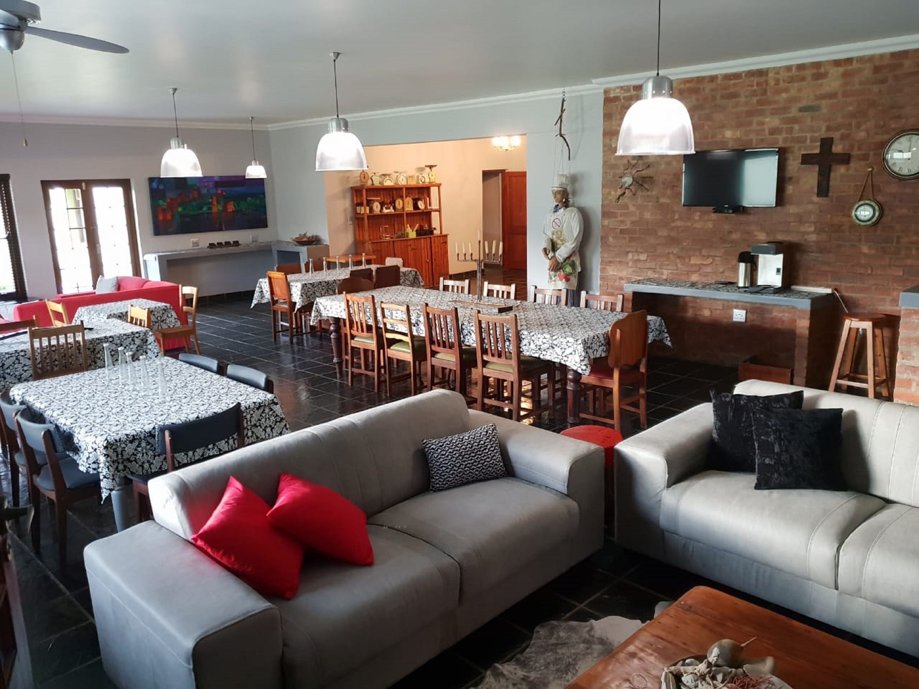 A spacious living area with a dining table, sofas, and a kitchen area with a brick wall and a TV.