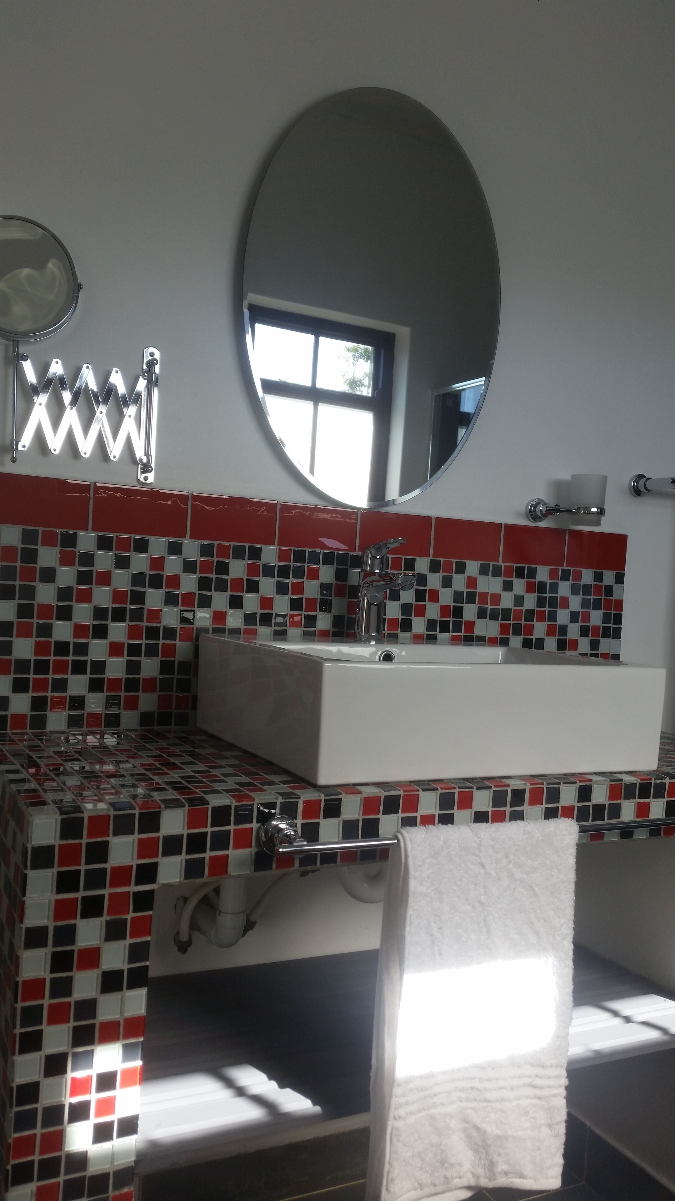 A bathroom with a white sink, a mirror, and red and black tiled walls.