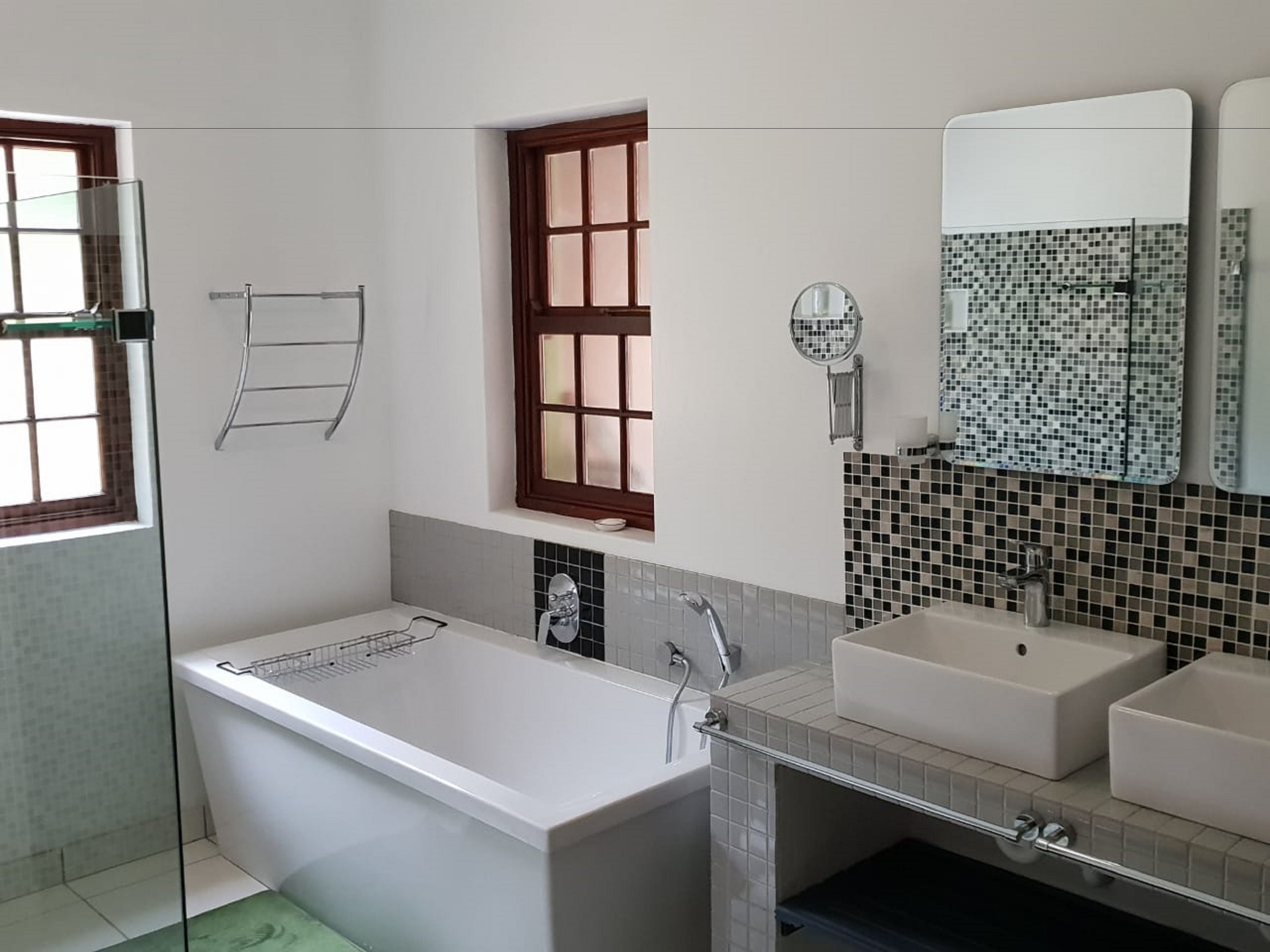 Een moderne badkamer met een bad, twee wastafels, een raam en een spiegel.