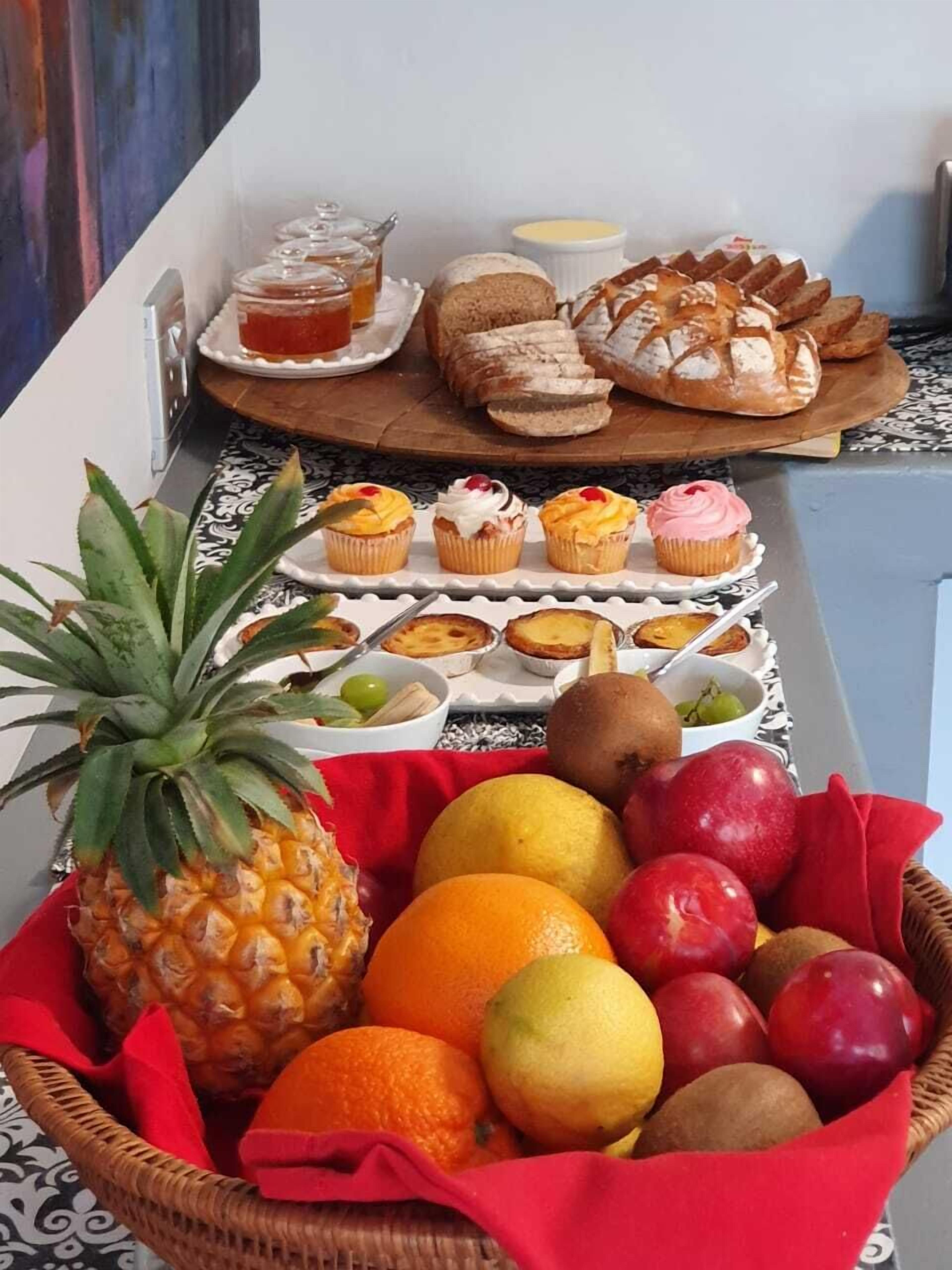 Una mesa con pasteles, pan y una cesta de frutas.