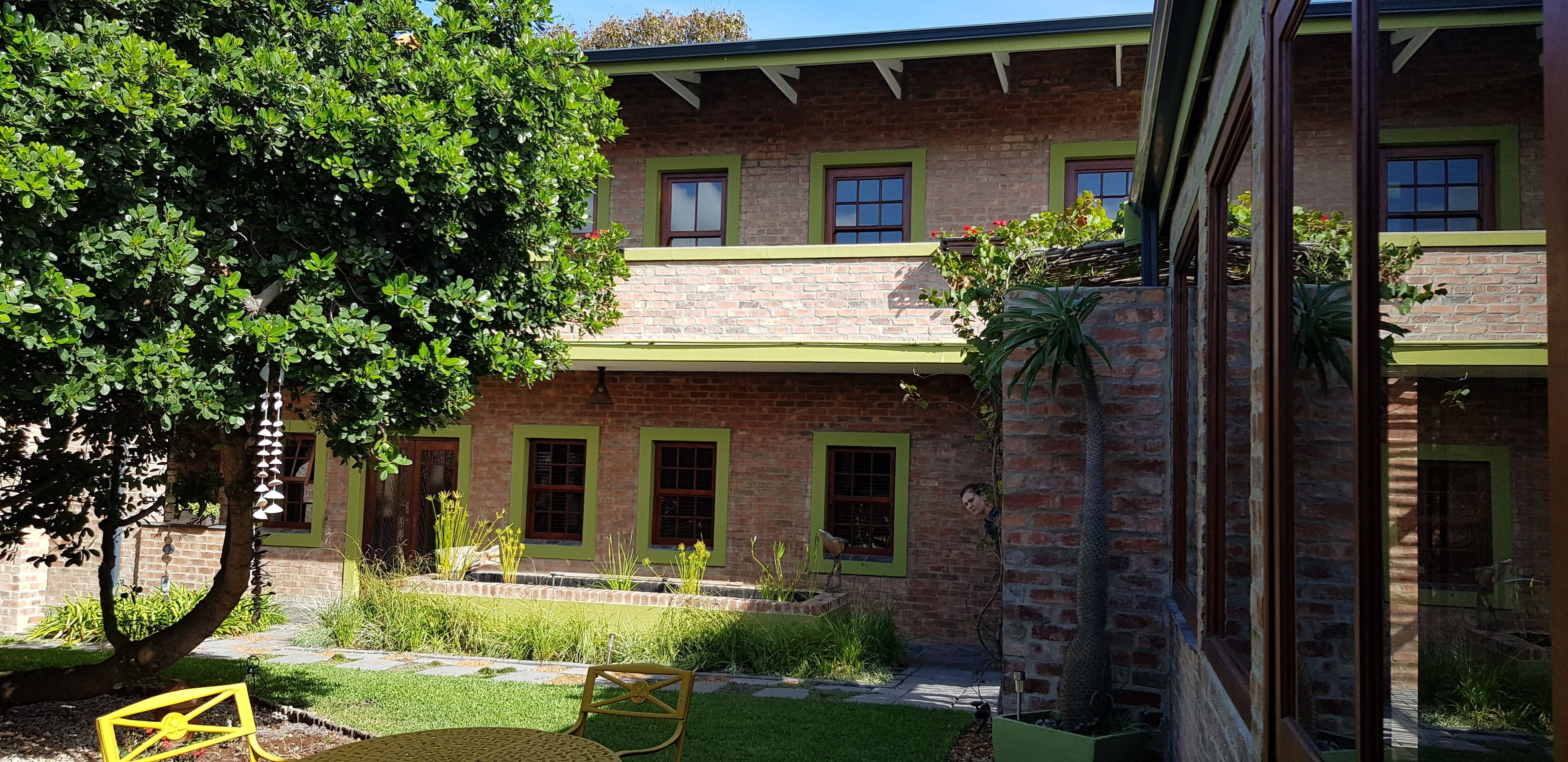 A brick building with green window frames, a tree, and a small garden area with a bench.