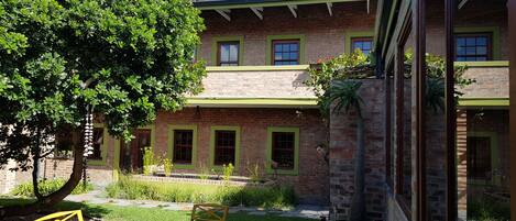 A brick building with green window frames, a tree, and a small garden area with a bench.