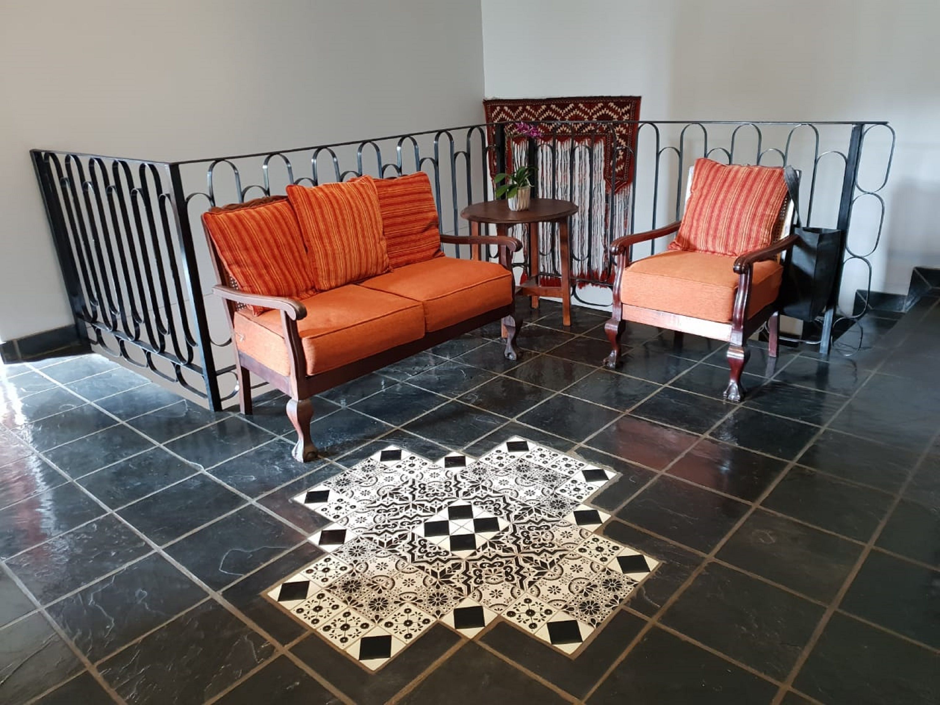 A room with a black and white patterned rug, an orange sofa, and two wooden chairs.