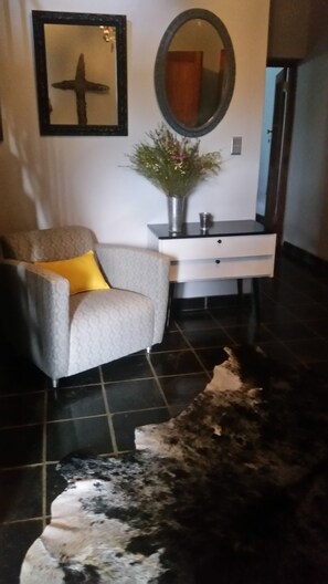 A living room with a sofa, a coffee table, a vase with flowers, a mirror, and a rug. - Port Del Mar Luxury Guesthouse (Hermanus)