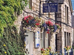 A stone building with a sign for 'The Well House' offering dinner, bed and breakfast, and rooms in suite. - The Well House (Pitlochry)