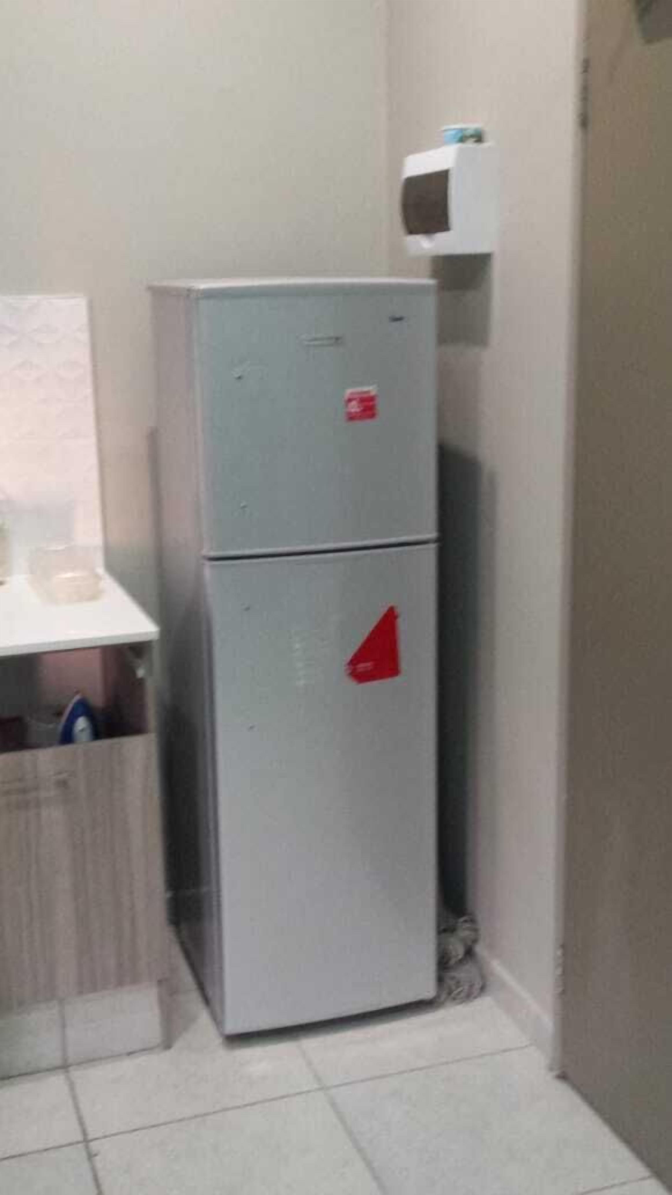 En liten, elektrisk spis med två kokplattor, placerad i ett hörn av ett rum med kakelgolv och en vit vägg.