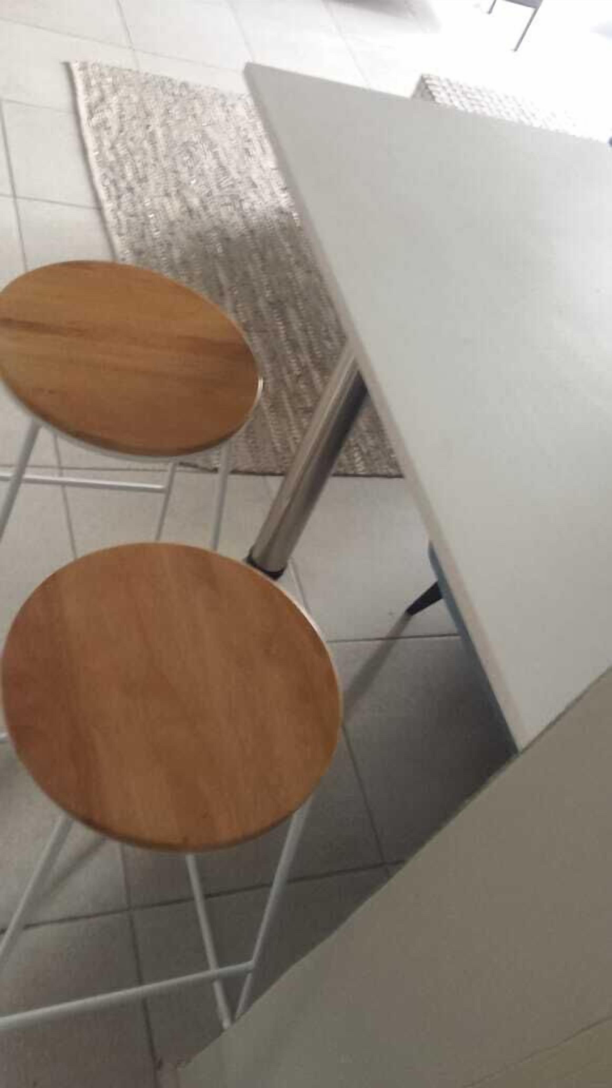 Een hoek van een kamer met een witte tafel en twee houten krukken.