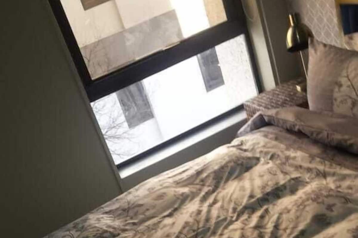 Ein Schlafzimmer mit einem Bett, einem Fenster und einem Nachttisch mit Lampe.