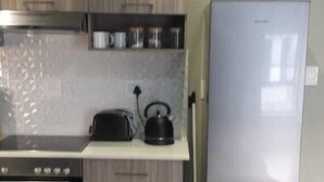 A compact kitchen with a built-in stove, a kettle, and a refrigerator. - Rosebank Accommodation (Johannesburg)