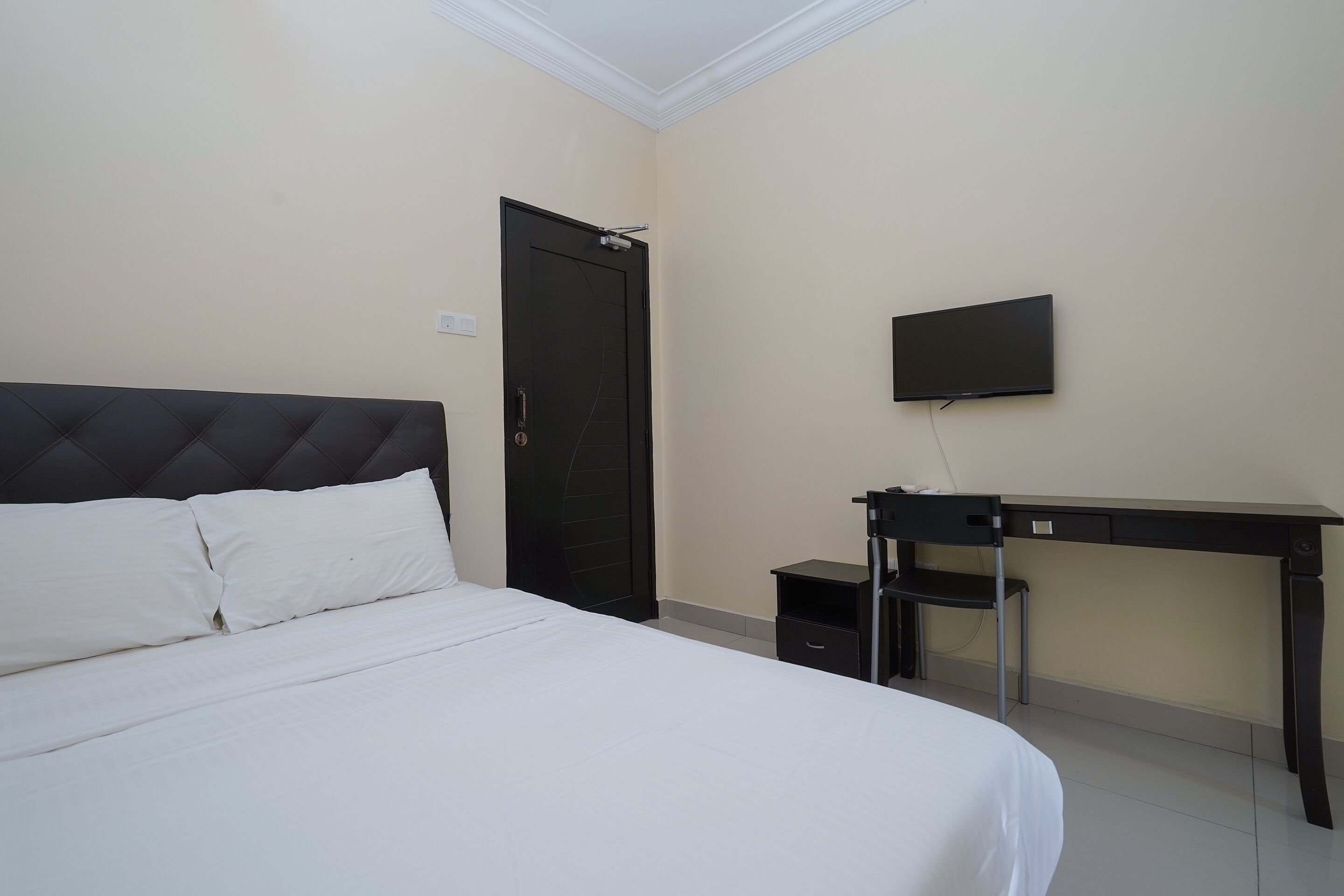 Een slaapkamer met een bed, een bureau, een stoel, een televisie en een deur.