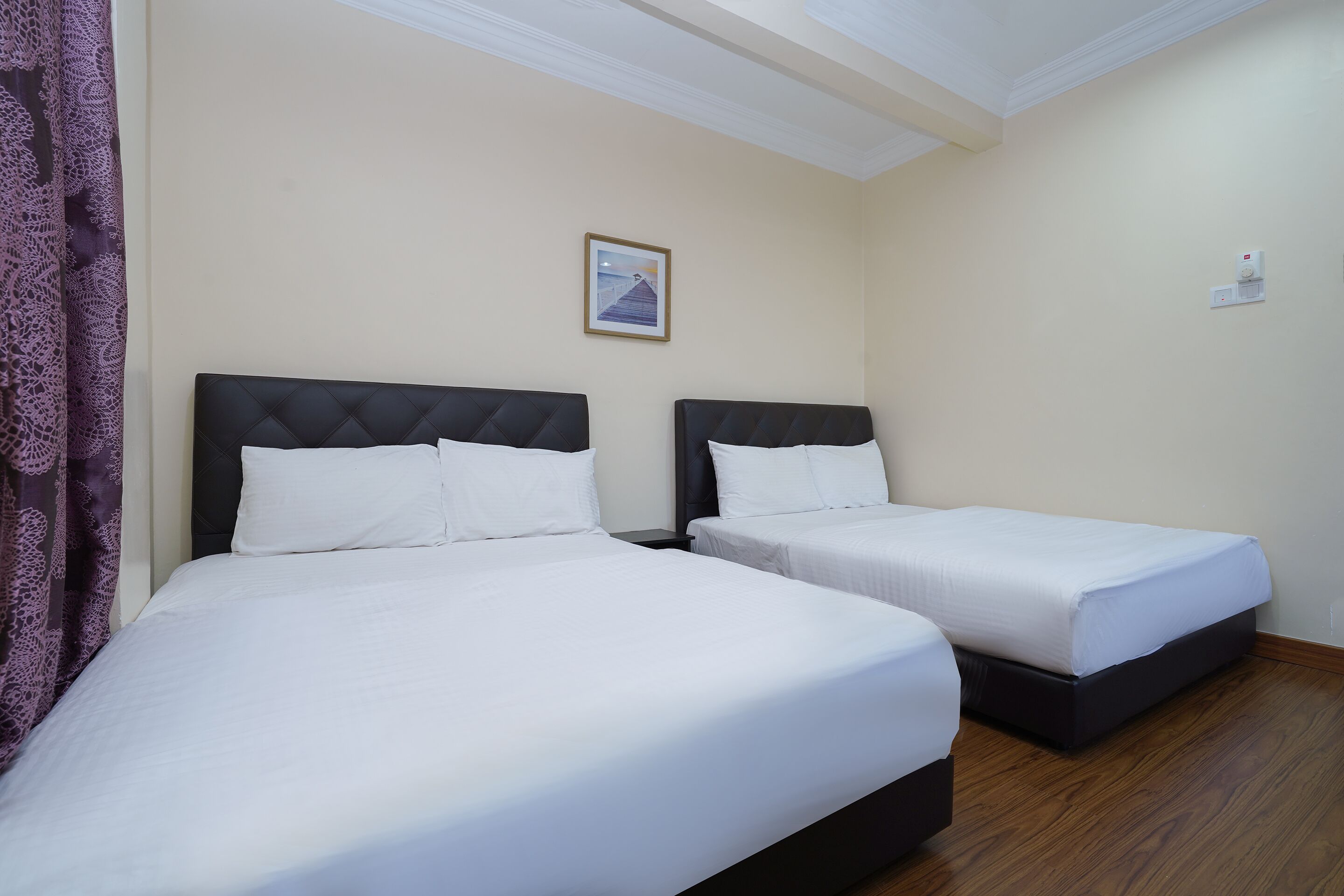 A hotel room with two beds, a ceiling with a decorative molding, a framed picture on the wall, and a thermostat on the wall.
