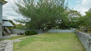 A backyard with a stone wall, a large tree, and a house with a staircase. - Hotel O Bangi Sri Minang Guesthouse (Bandar Baru Bangi)