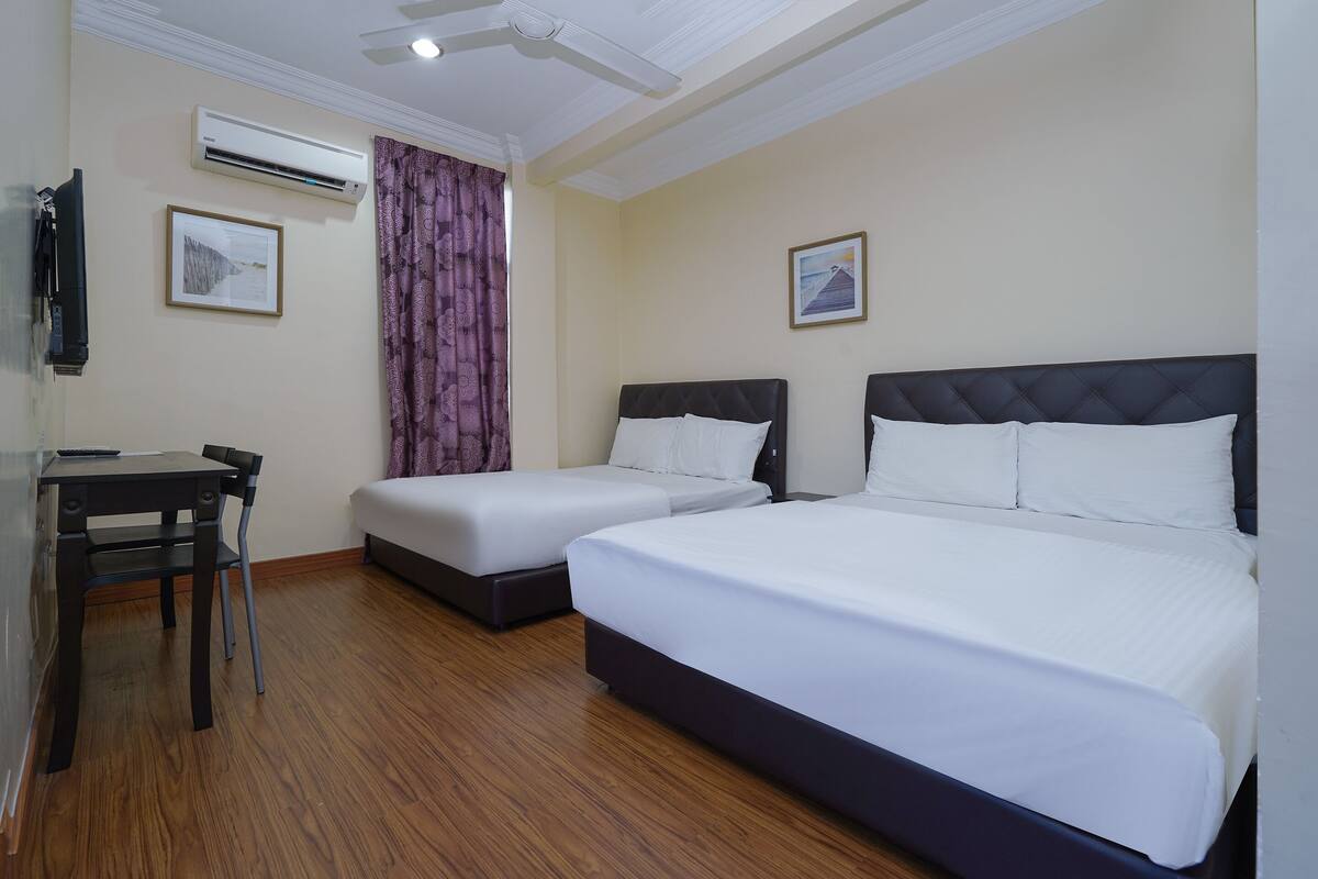 Ein Hotelzimmer mit zwei Betten, einem Schreibtisch, einem Sessel, einer Klimaanlage und zwei gerahmten Bildern an den Wänden.