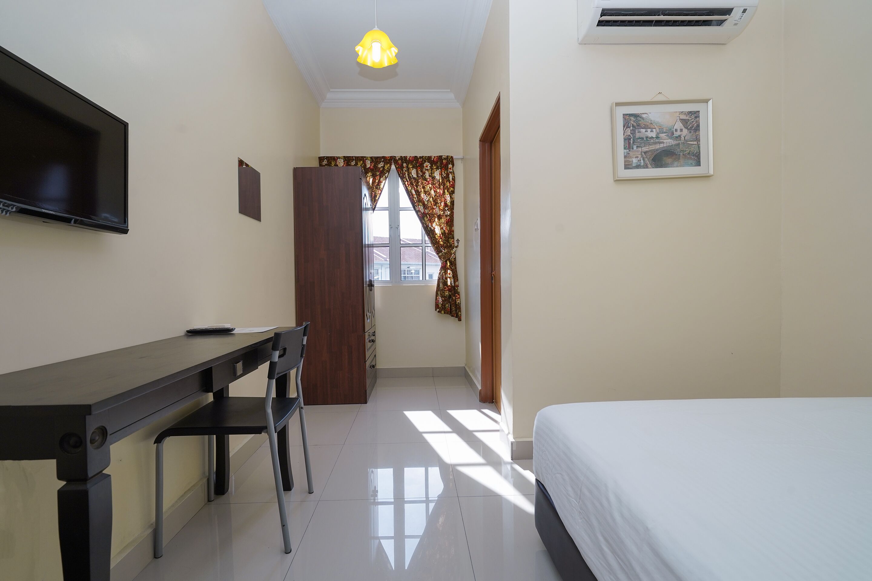 A hotel room with a bed, a desk, a chair, a TV, a picture on the wall, and a window with curtains.