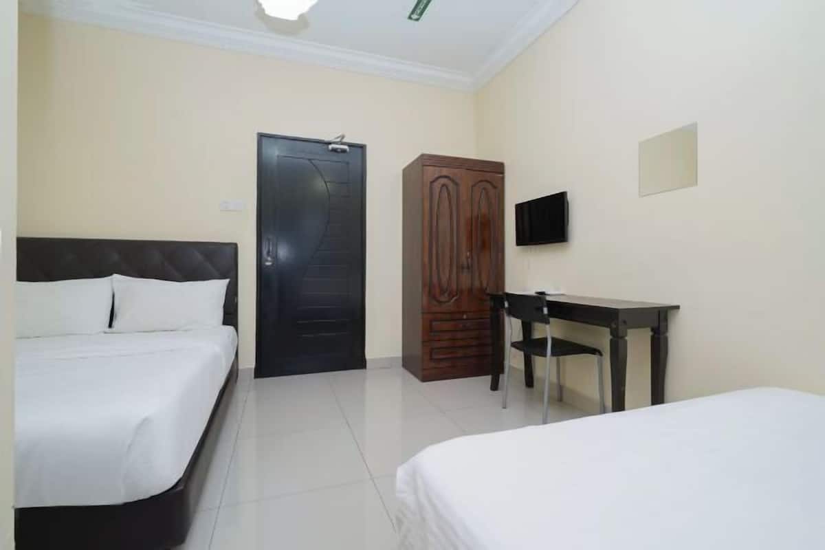 Ein Hotelzimmer mit zwei Betten, einem Schreibtisch, einem Kleiderschrank und einem Fernseher an der Wand.