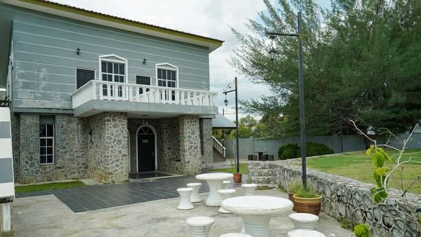 A two-story house with a stone facade, a balcony, and a paved patio with white stone tables and chairs. - Hotel O Bangi Sri Minang Guesthouse (Bandar Baru Bangi)