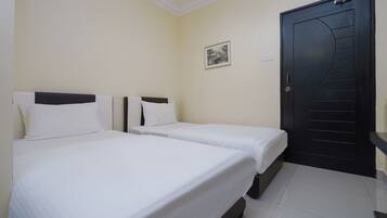 A hotel room with two single beds, a black door, and a small framed picture on the wall.