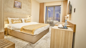 Een hotelkamer met een groot bed, een bureau met een lamp, een waterfles en uitzicht op de stad door het raam.