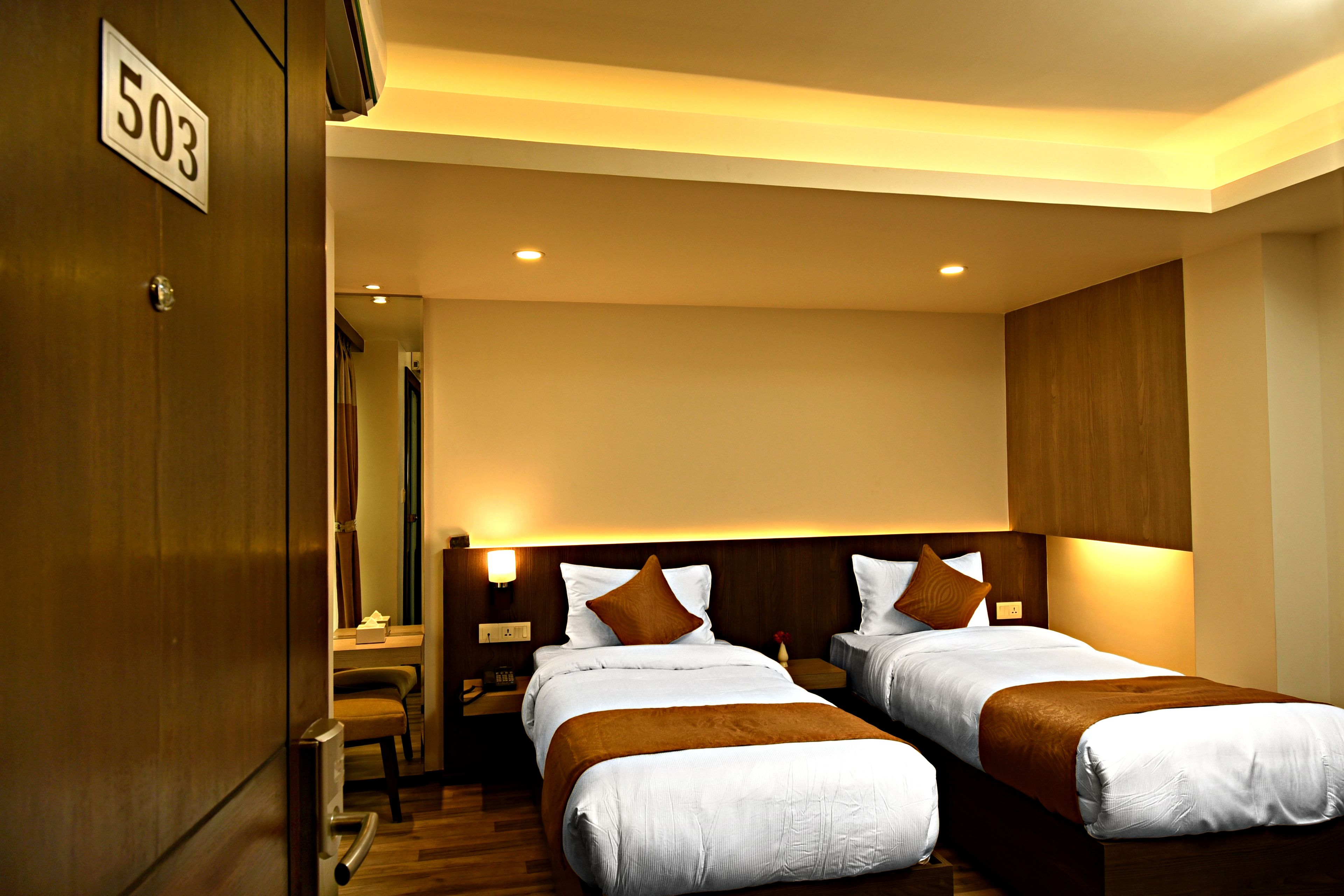 Une chambre d’hôtel avec deux lits, une porte en bois portant un numéro et un petit bureau avec une chaise.