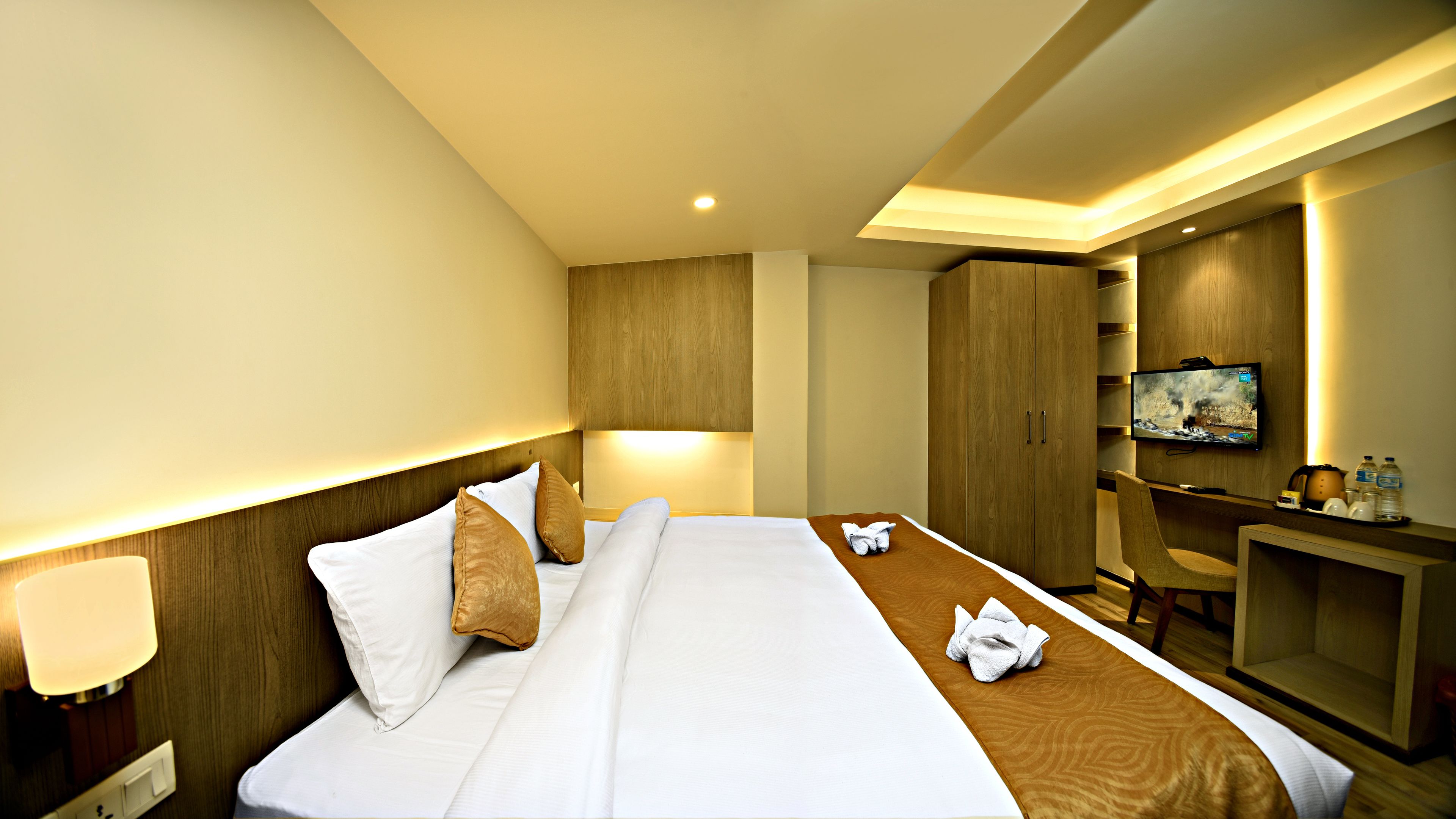 A hotel room with a bed, a desk, a TV, and a wardrobe.