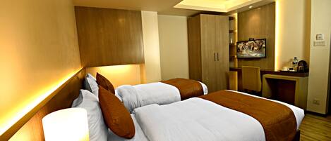 Habitación de hotel con dos camas, un escritorio, un televisor y una obra de arte colgada en la pared.