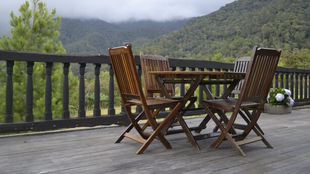 Una terraza de madera con una mesa y cuatro sillas, con vistas a un paisaje montañoso.