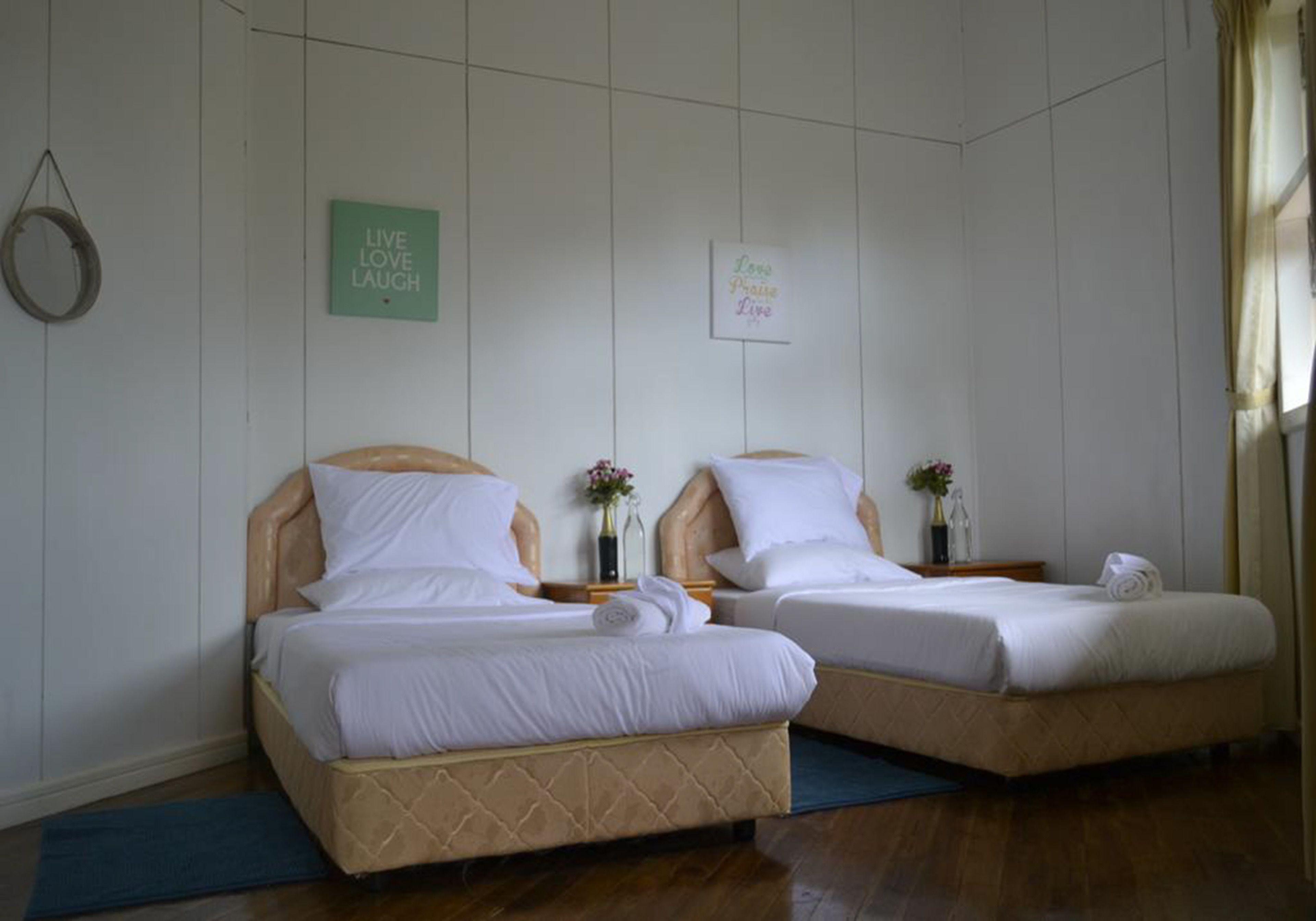 Zwei Einzelbetten mit Holz-Kopfteilen und weißer Bettwäsche in einem Zimmer mit weißen Wänden und Holzboden.
