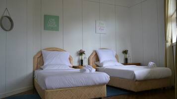 Zwei Einzelbetten mit Holz-Kopfteilen und weißer Bettwäsche in einem Zimmer mit weißen Wänden und Holzboden.