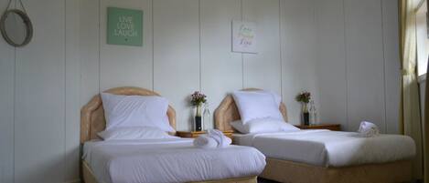 Zwei Einzelbetten mit Holz-Kopfteilen und weißer Bettwäsche in einem Zimmer mit weißen Wänden und Holzboden.