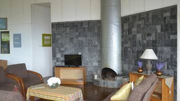 Ein gemütliches Wohnzimmer mit Kamin aus Stein, bequemen Sitzgelegenheiten und einem Fernseher auf einem Holzständer.