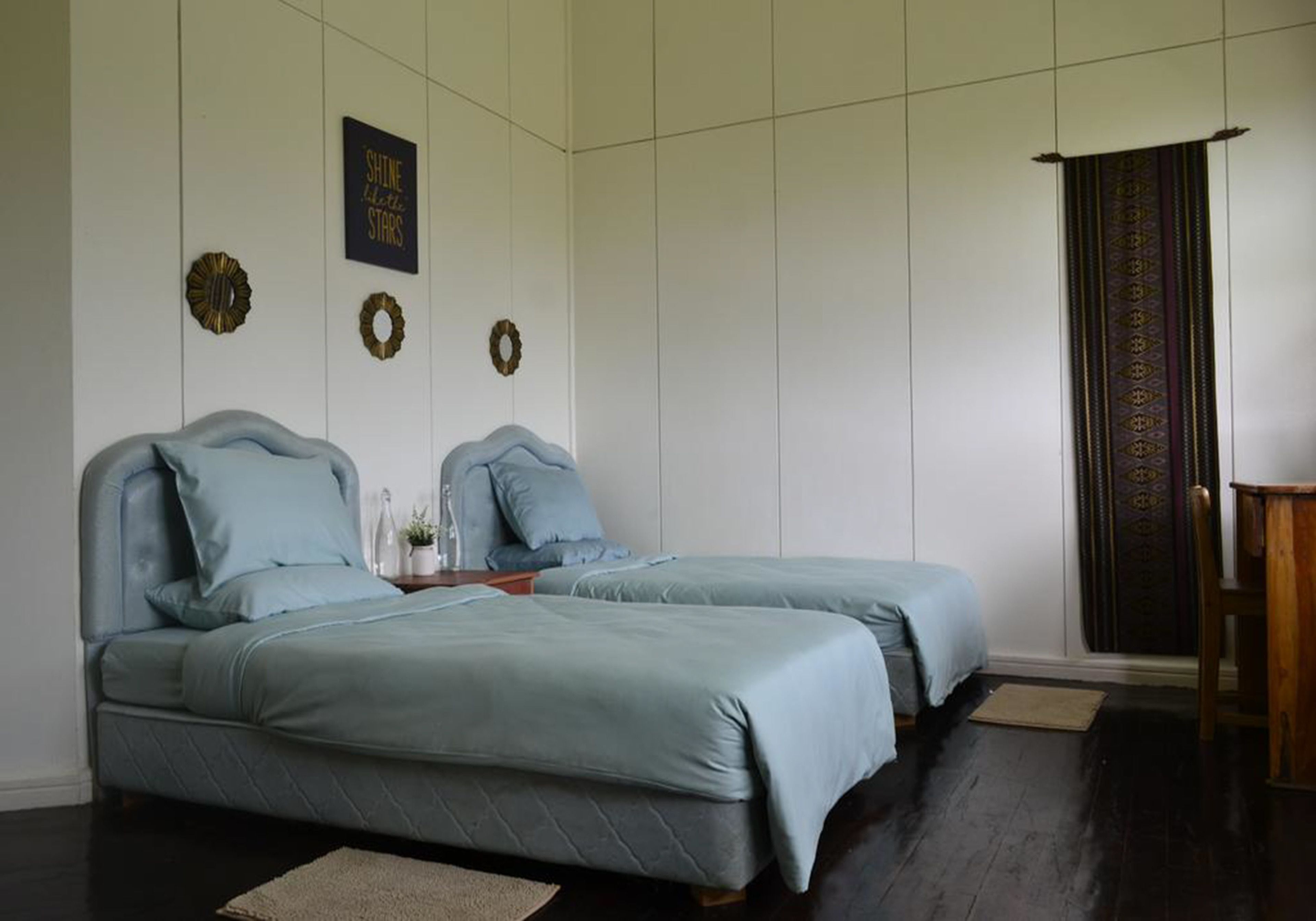 A bedroom with two beds, a dark wooden floor, a small rug, and a decorative wall hanging.