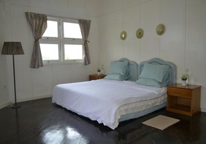 Ein Schlafzimmer mit einem großen Bett, zwei Nachttischen, einer Stehlampe und einem Fenster mit Vorhängen.