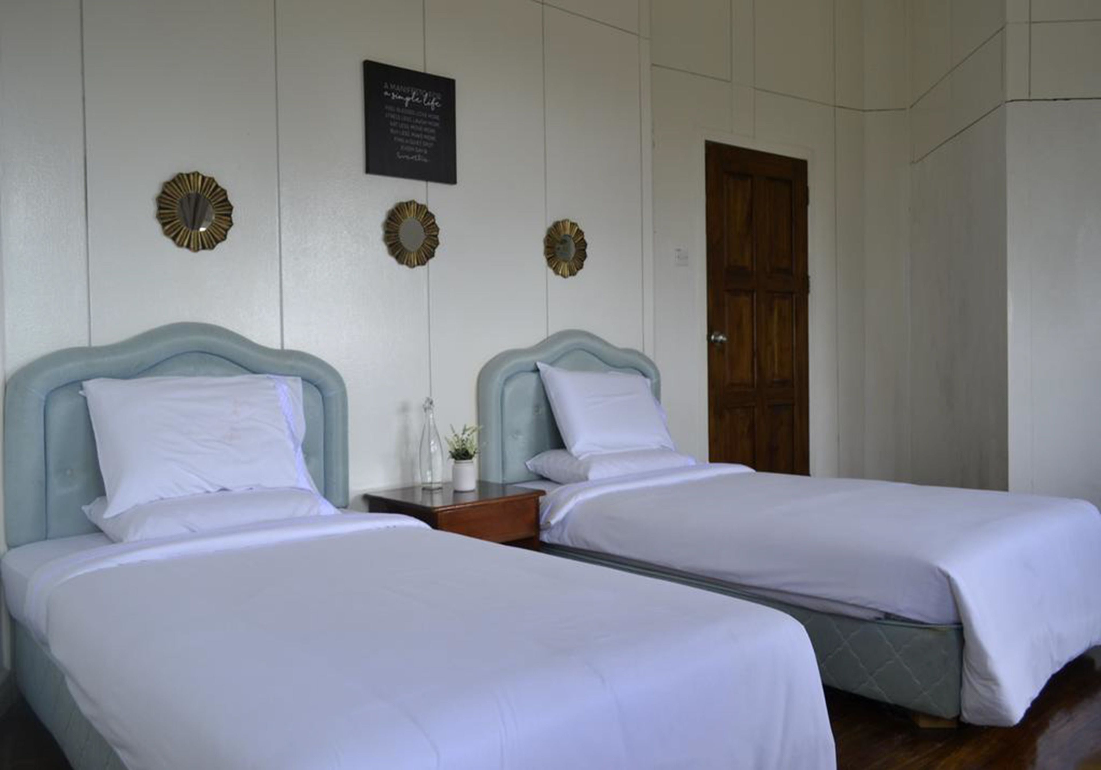 Ein Hotelzimmer mit zwei Einzelbetten, einer Holztür und dekorativen Wandspiegeln.