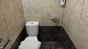 Une petite salle de bain carrelée, équipée de toilettes, d’une douche et d’un sèche-mains.