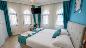 Une chambre d’hôtel avec un grand lit, un téléviseur à écran plat, une table de chevet avec une bouilloire et des rideaux.