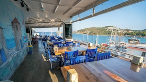 Un restaurant avec des chaises et des tables bleues, une fresque murale et une vue sur la mer et les bateaux.
