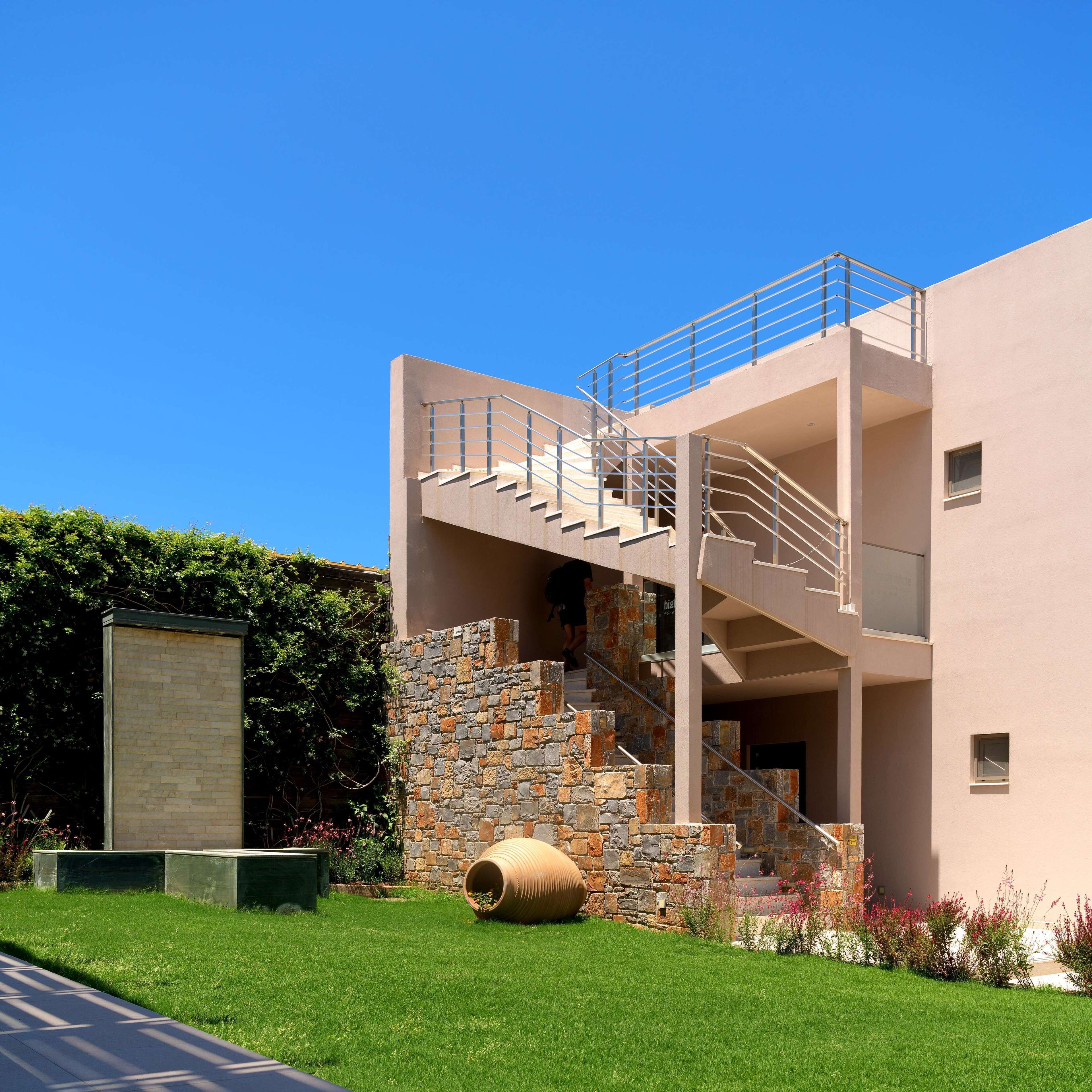 Un edificio moderno con una escalera de piedra que conduce a un nivel superior, rodeado de un césped cuidado y una jardinera grande.